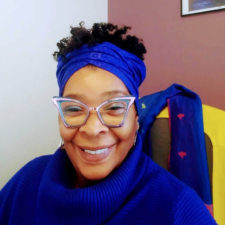 Raffini in a blue sweater and headscarf smiling into the camera